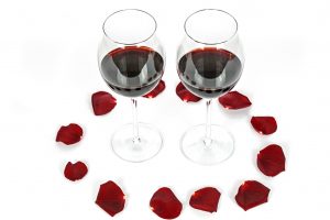 Two glasses of wine surrounded by red rose petals